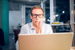 © Svyatoslav Lypynskyy - Office worker staying up late working.Portrait of businessman with square glasses sitting behind computer looking straight into camera with his hands near his face.