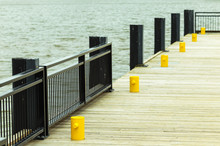 Sea Pier With Wooden Floor, Yellow Metal Bollard And Black Metal Railings