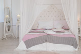 Fototapeta Uliczki - Big bed with cute pastel bedding in woman's room. Modern bedroom in pastel colors. four-poster bed.Scandinavian simplicity design. Eco loft apartments.