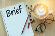 Concept Brief on notebook with glasses, pencil and coffee cup on wooden table