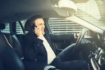 Wall Mural - Smiling businessman talking on a cellphone in his car