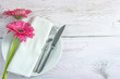Festive table setting: purple gerbera flowers, cutlery and napkin on white plate