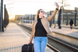 © terovesalainen - Woman taking selfie with mobile phone in train platform at station. Smiling and happy lady taking photo of herself with smartphone. Traveler and tourist arrived to destination.
