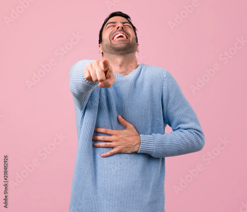 Fotografía Handsome man pointing with finger at someone and laughing a lot on pink backgrou
