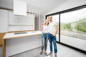 Happy couple standing together enjoying their new modern house with big window and green area outdoors