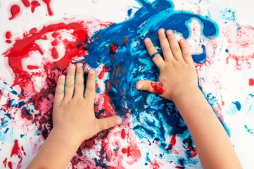 Painted hands smudging colors on messy paper