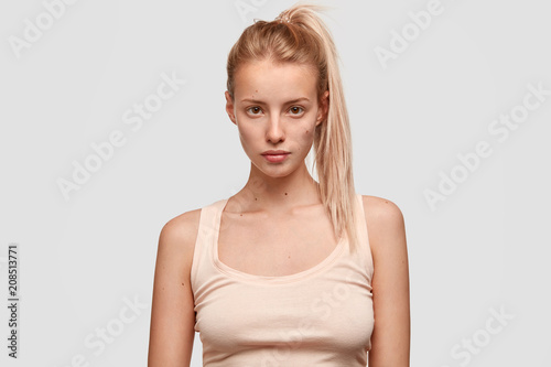 Fotografiet Indoor view of pleasant looking sportswoman with pony tail, dressed in casual t shirt, rests indoor after jogging, has confident expression, isolated over white background