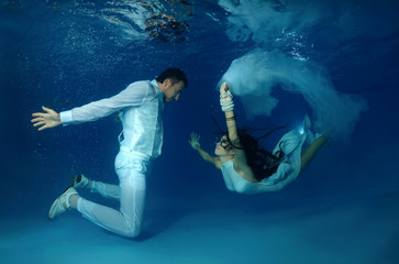 Bride and groom in a white wedding dress swim to each other underwater in the pool. Underwater wedding