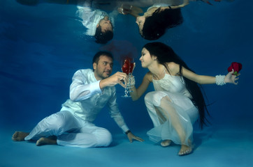 Bride and groom drink red wine underwater in the pool. Underwater wedding