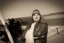 Portrait Of A Vintage Pilot With Leather Cap, Scarf And Aviator Glasses In Front Of A Historic Airplane Biplane - Portrait Of A Man In Historical Pilot Clothing - Vintage Old Picture Style
