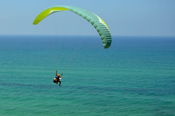 man is flying on green paraglider in the sky above the azure sea. .Balance, extreme sports, active lifestyle. Mediterranean Sea, Israel