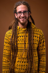 Young handsome Hispanic man with dreadlocks against brown backgr