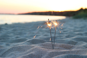 Bengal lights on the sand near the sea on a sunset background