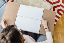 Woman unboxing cardboard box online e-commerce site delivery  - view from above in living room