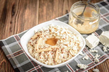 Wall Mural - Homemade oatmeal with honey, peanut butter, peanut, flax seeds and cottage cheese on wooden background. Healthy breakfast.