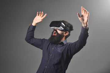 Emotional bearded man wears virtual reality goggles, gesturing with hands. Connection, future technology, new generation, progress concept. Virtual reality glasses, entertainment. Man using VR headset