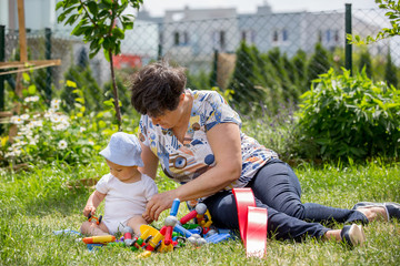 Wall Mural - Little baby boy, playing with his grandmother with big construction blocks in garden building shapes