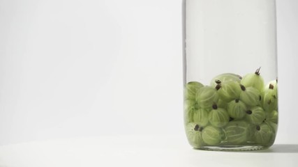 Aufkleber - Green gooseberry in glass bottle on a white round wooden table, rotation 360 degrees. Beautiful white background.