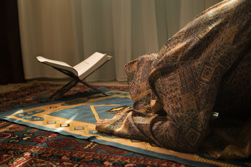 Wall Mural - Muslim woman praying for Allah muslim god at room near window. Hands of muslim woman on the carpet praying in traditional wearing clothes, Woman in Hijab, Carpet of Kaaba, Selective focus, toned