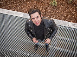 Young handsome man standing on metal grid looking at camera, seen from above in city environment