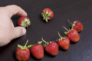 The man puts the strawberry in the shape of a smiley face. On a dark table.