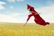 © Creativa Images - Asian woman ballerina holding red fabric making a big jump on meadow.