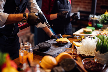 Chef preparing delicious burger melting cheese on black bun.