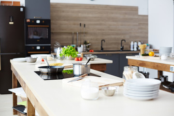 Workplace of chef with pan and frying-pan on electric stove and kitchenware on table