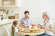 © pressmaster - Young parents and little daughter sitting by served table, eating breakfast and talking