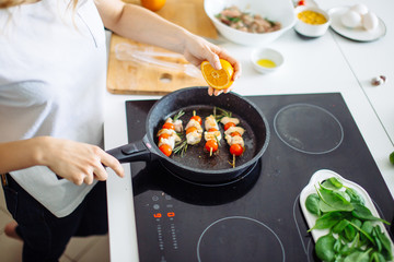 Wall Mural - Cropped view of young happy housewife frying chicken meat with orange juice for dinner on glass-ceramic stove.