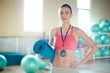 © pressmaster - Young fitness trainer in activewear carrying rolled blue mat while going to working out