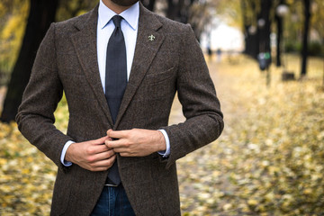 Man in custom tailored suit posing outdoors in autumn and buttoning his coat