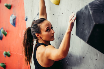 Wall Mural - Comcentrated young woman looking up choosing the route, climbing on rock artificial wall.