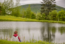 Boy With A Fishing Rod Sits On The Shore Of A Mountain Lake. Young Fisherman. Copy Space For Your Text