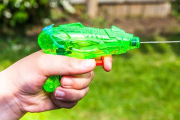 Child playing with a green water pistol in a garden