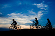 Friends riding bicycles at sunset sky. Silhouettes of three students cycling on hill on evening sky background. People and active leisure.