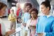 © pressmaster - Content confident female administrator writing names of forum participants in list while talking to them in corridor, people using gadgets and standing in line