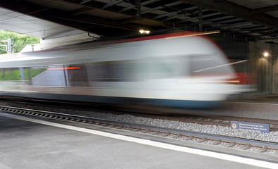 Wall Mural - Train speeding through a swiss station captured as a motion blur