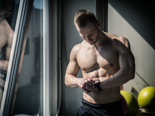 Young topless attractive man in gym checking sports watch to track his workout, heart pulse or fitness