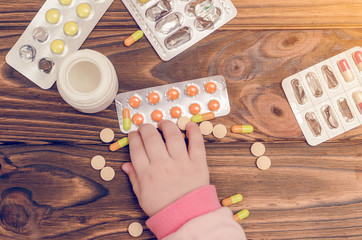 Children's hands with medicines on a wooden table. A small child left unattended plays dangerous drugs