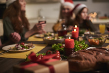Focus of festive table decorated with candles for Christmas. Two women are sitting at background with kid eating vegetables and drinking red wine