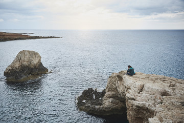 Wall Mural - Nature calming down everyone. Peaceful girl is sitting on stone cliff and enjoying the sea view. Beautiful landscape concept 