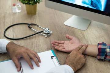 Hand of a doctor checking the pulse on a male patient at a desk in the hospital.