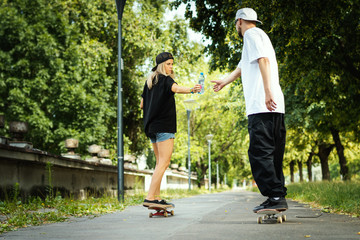 man and a woman are going on a skateboard and give themselves water on a summer day