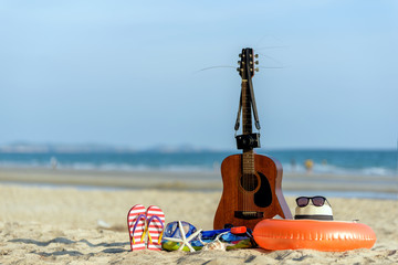 Classic guitar and beach accessories on white sandy beach with blue sky .Vacation ,Summer , Holiday ,Travel ,Relaxing concept.