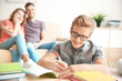 © Africa Studio - Teenager doing homework while parents sitting on sofa at home