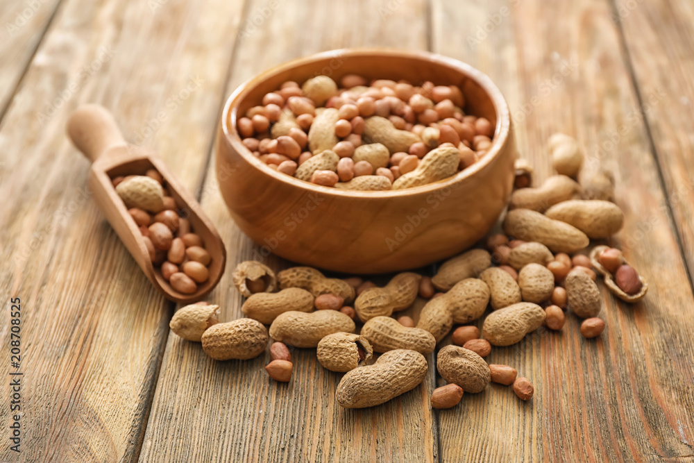 Bowl and scoop with tasty peanuts on wooden table