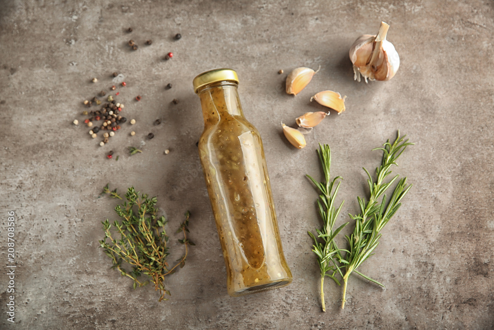 Bottle with tasty sauce and herbs on grey background, flat lay