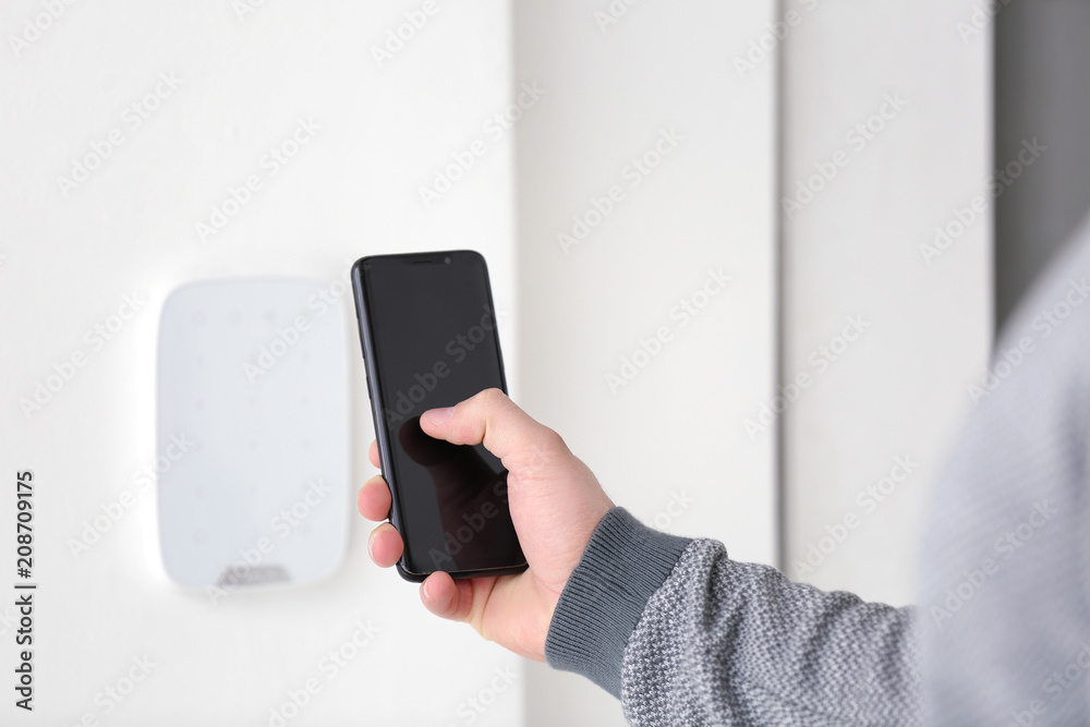 Young man setting alarm system with mobile phone, indoors