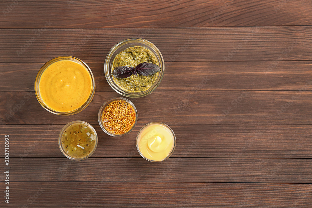 Bowls with different sauces on wooden background, top view